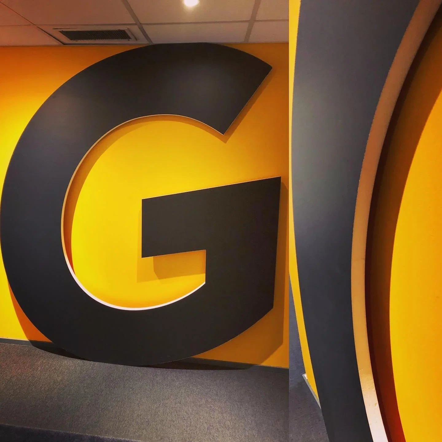 Large black 3D letter G wall sign on yellow background, indoor commercial space