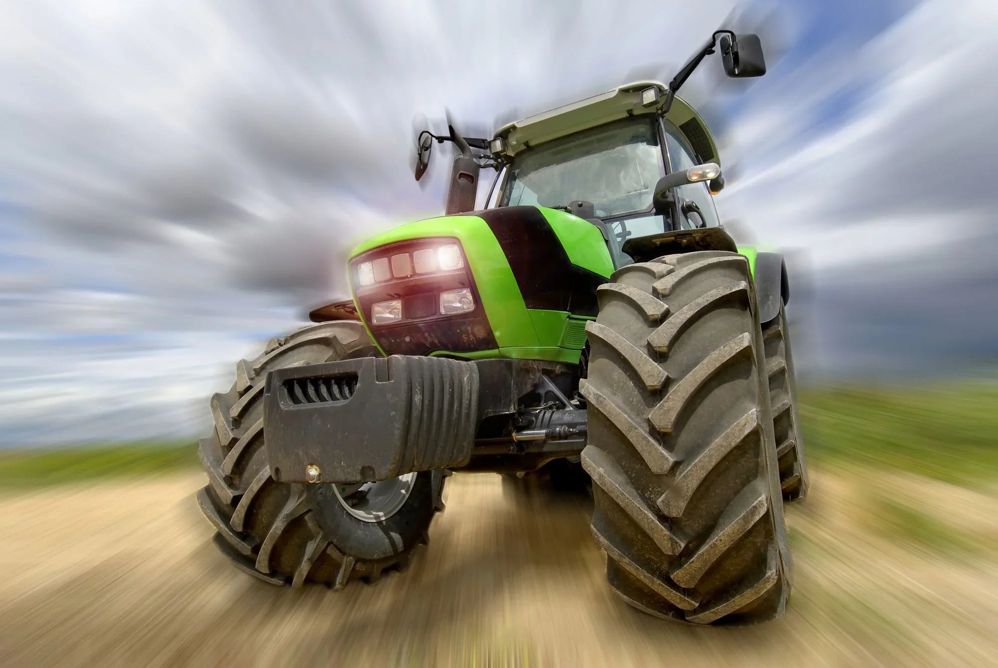 Green agricultural tractor with large tires on a dirt road, motion blur effect