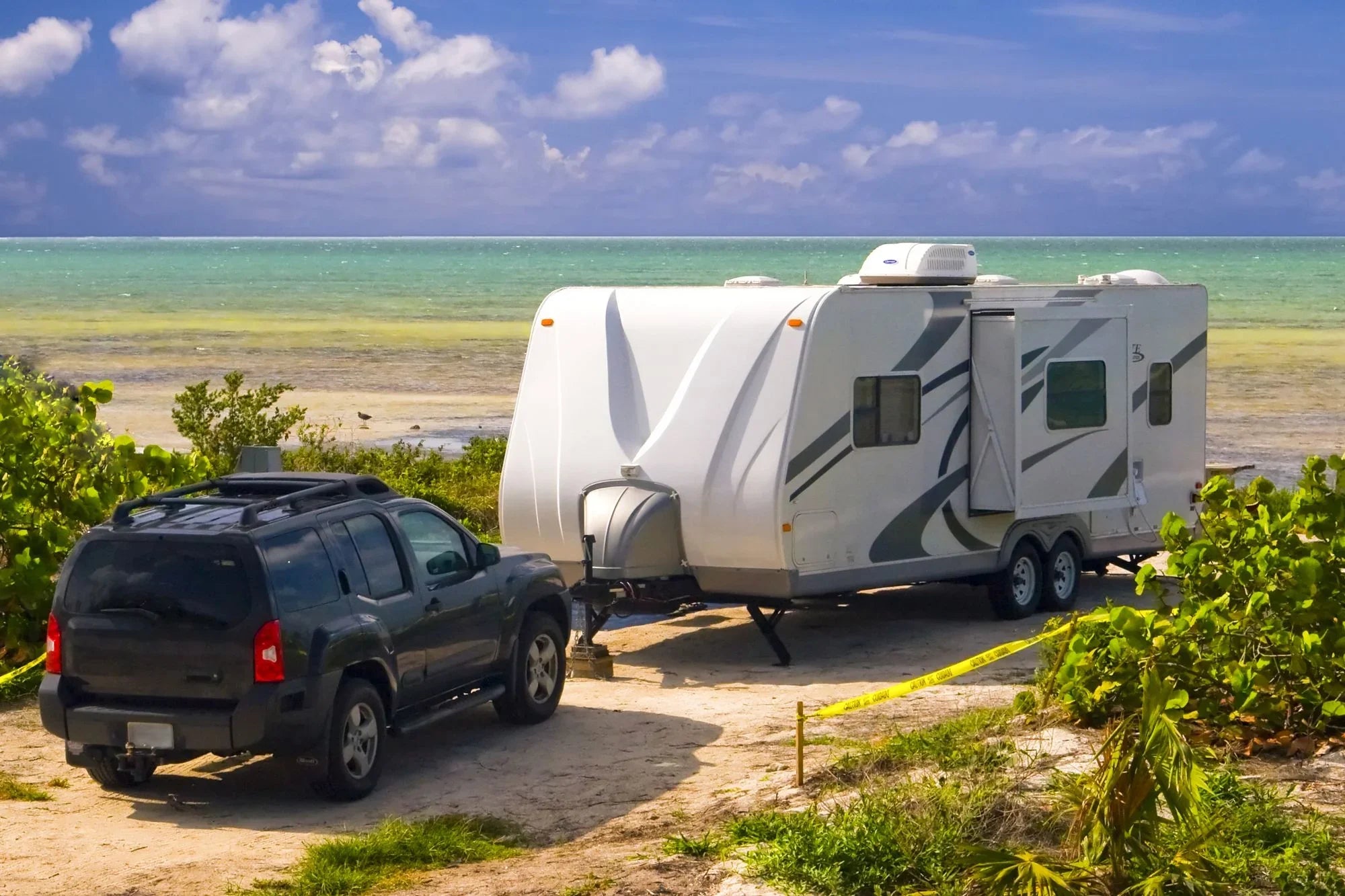 SUV towing a white travel trailer next to the sea, tropical beach setting