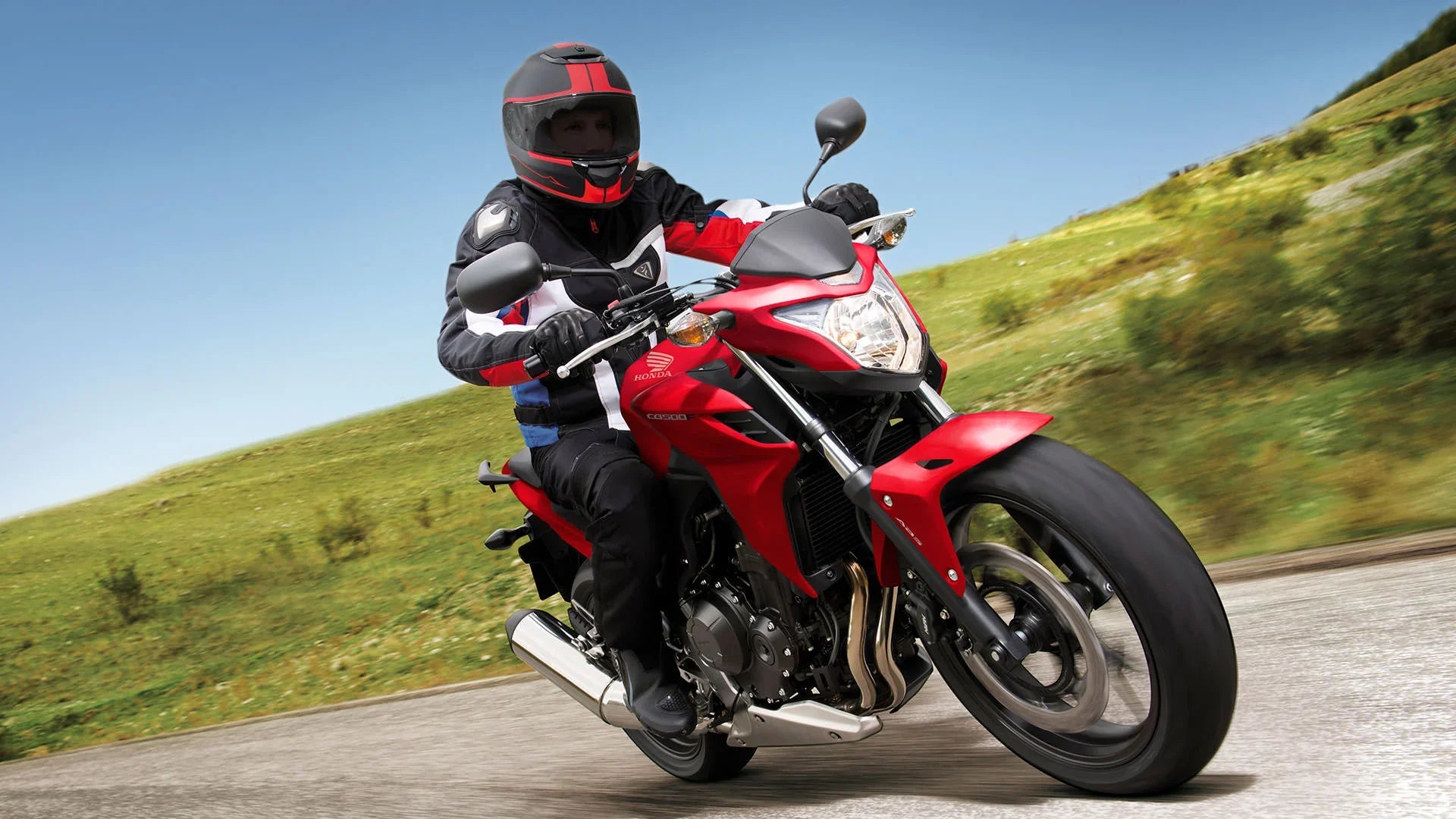 Person riding a red Honda motorcycle on a road, wearing helmet and protective gear