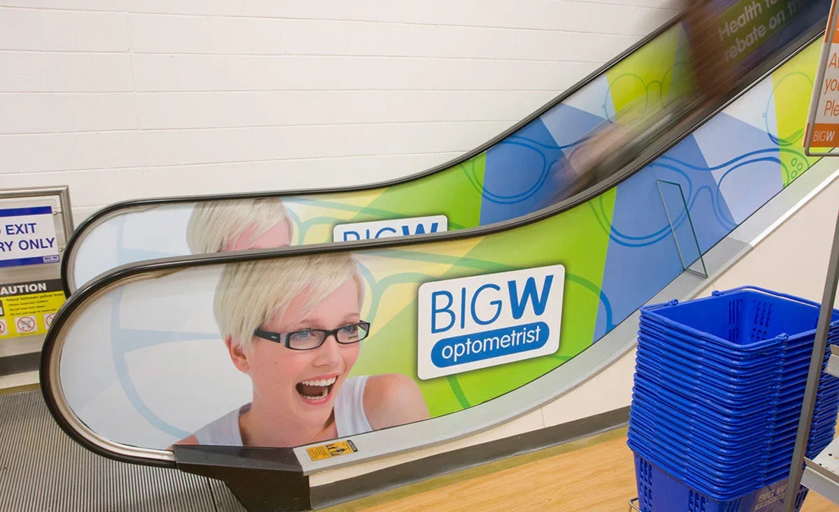 Escalator with colorful advertising sticker, smiling person, and shopping baskets nearby.
