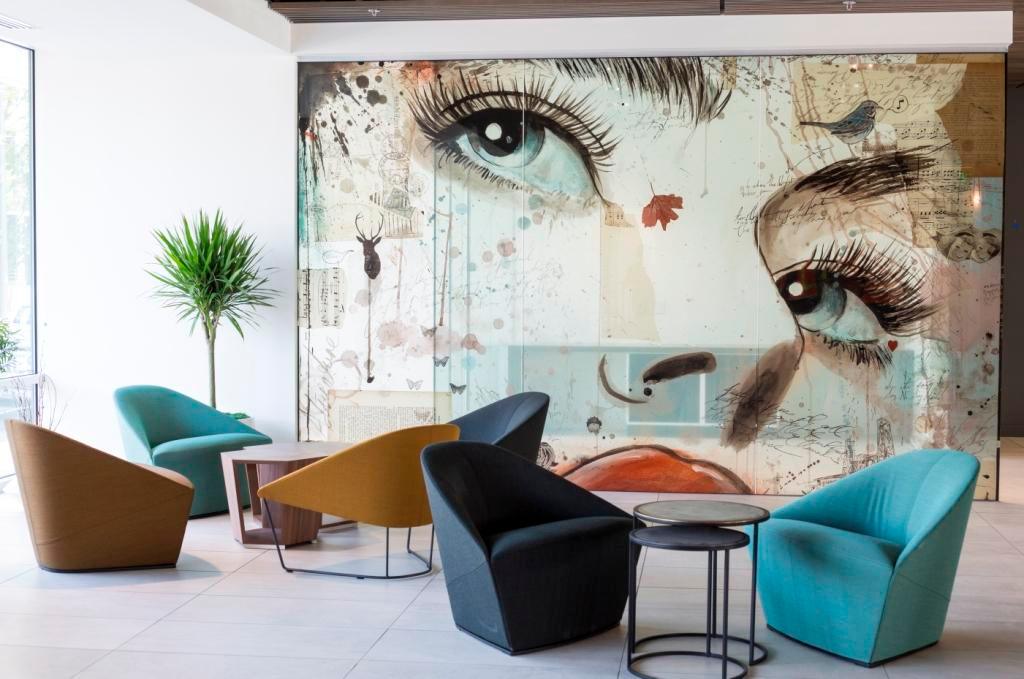 Modern lobby with colorful lounge chairs and large artistic wall mural featuring expressive eyes