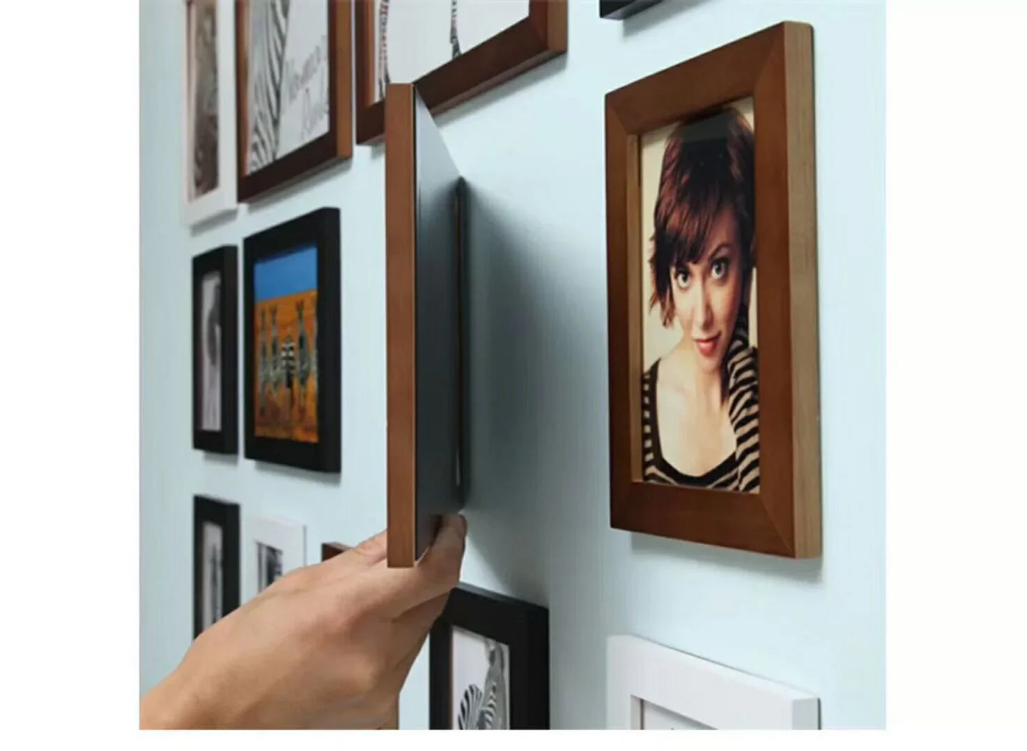 Hand mounting a wooden photo frame with magnetic wall fixing system among gallery wall frames